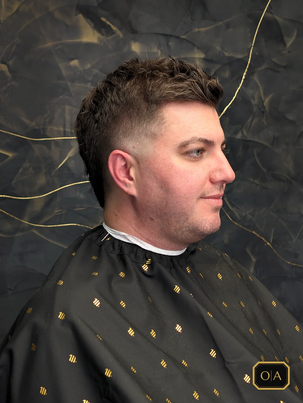 A finished burst fade curving around the ear with a textured brush-up on top, seen from the side against the shop's black wall