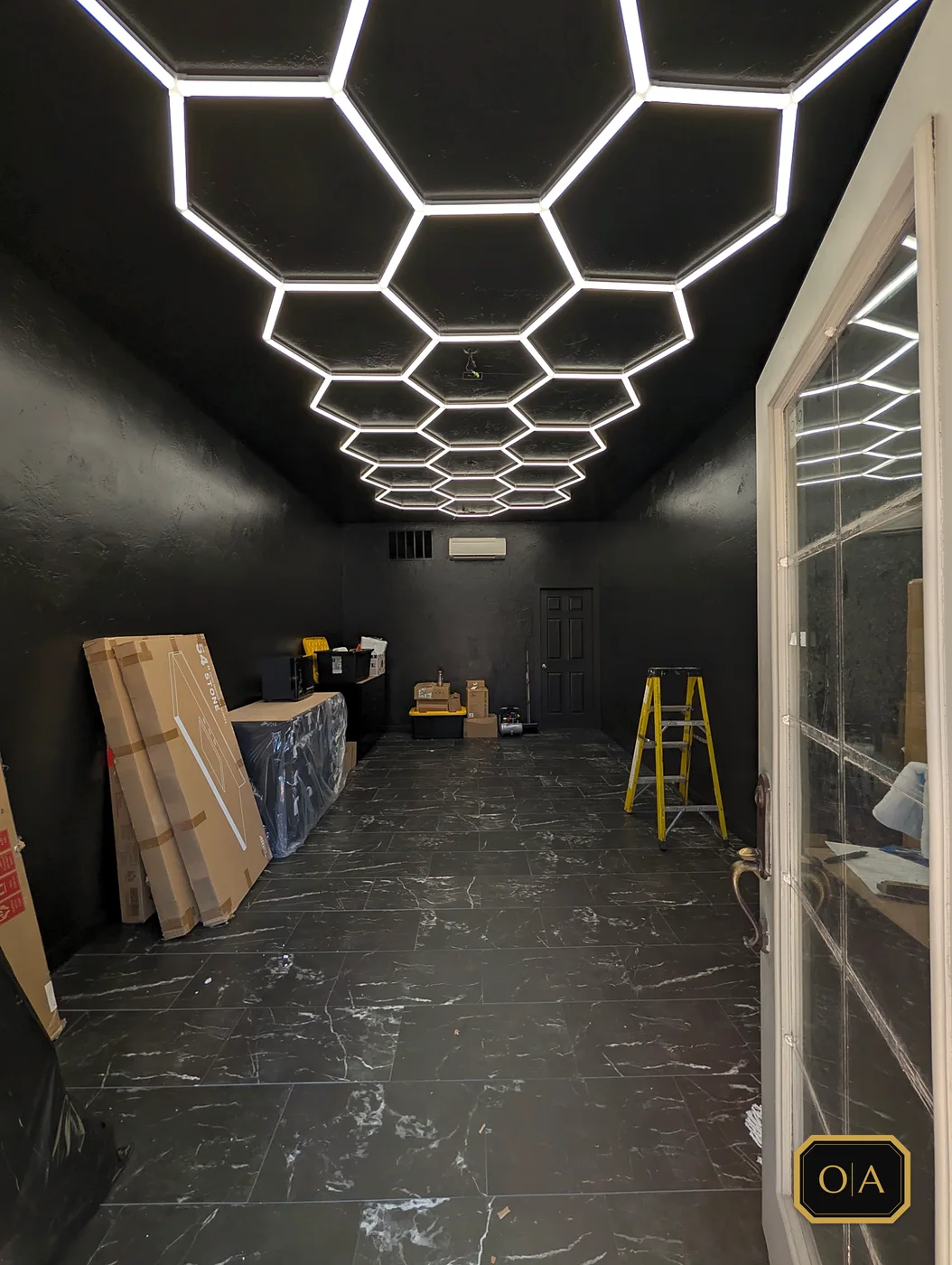 The same room with the hexagon light grid up and the black marble-look floor down, fixture boxes still waiting along the wall.